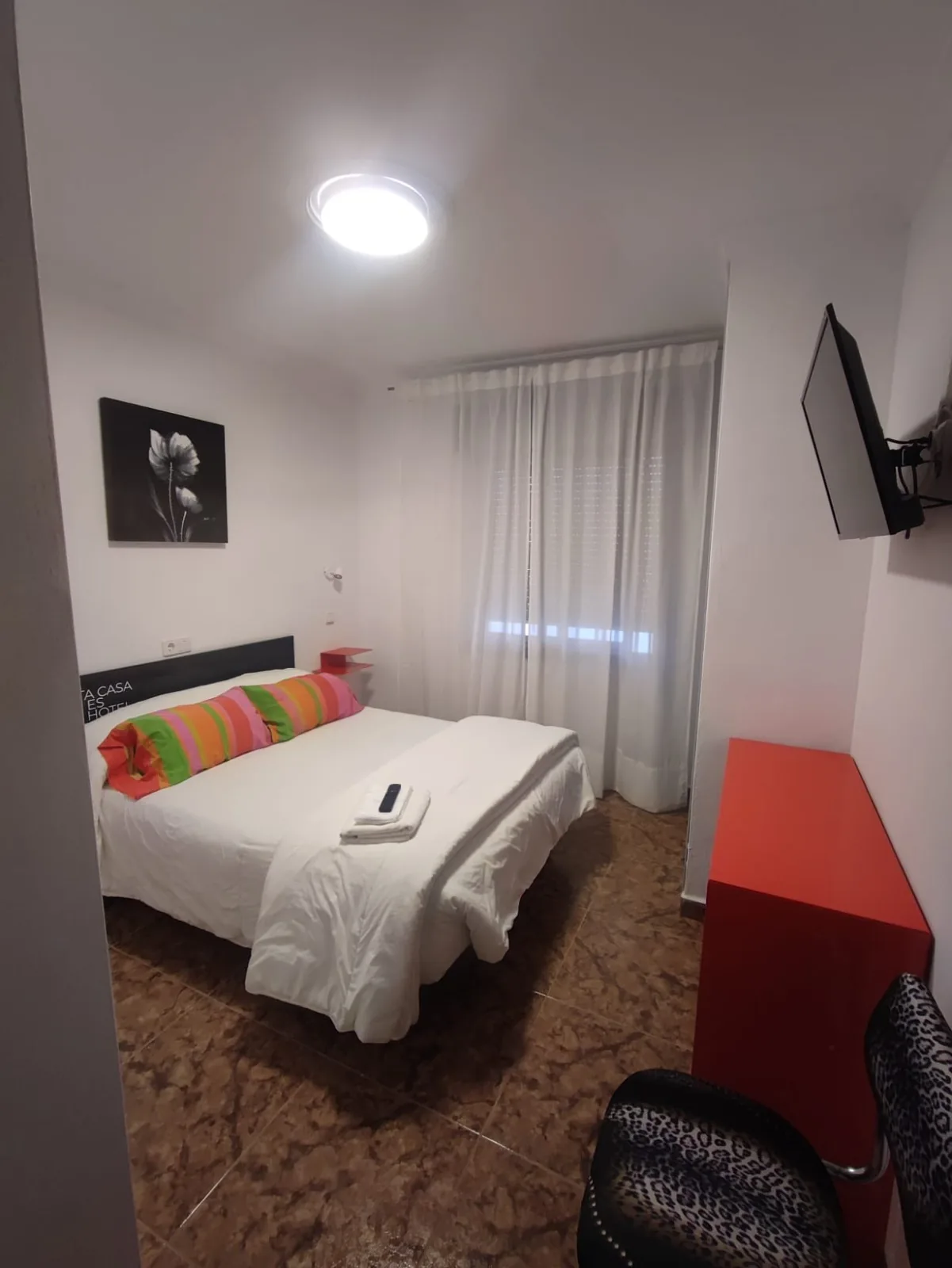 Habitación con cama doble, televisor de pared y cortinas blancas