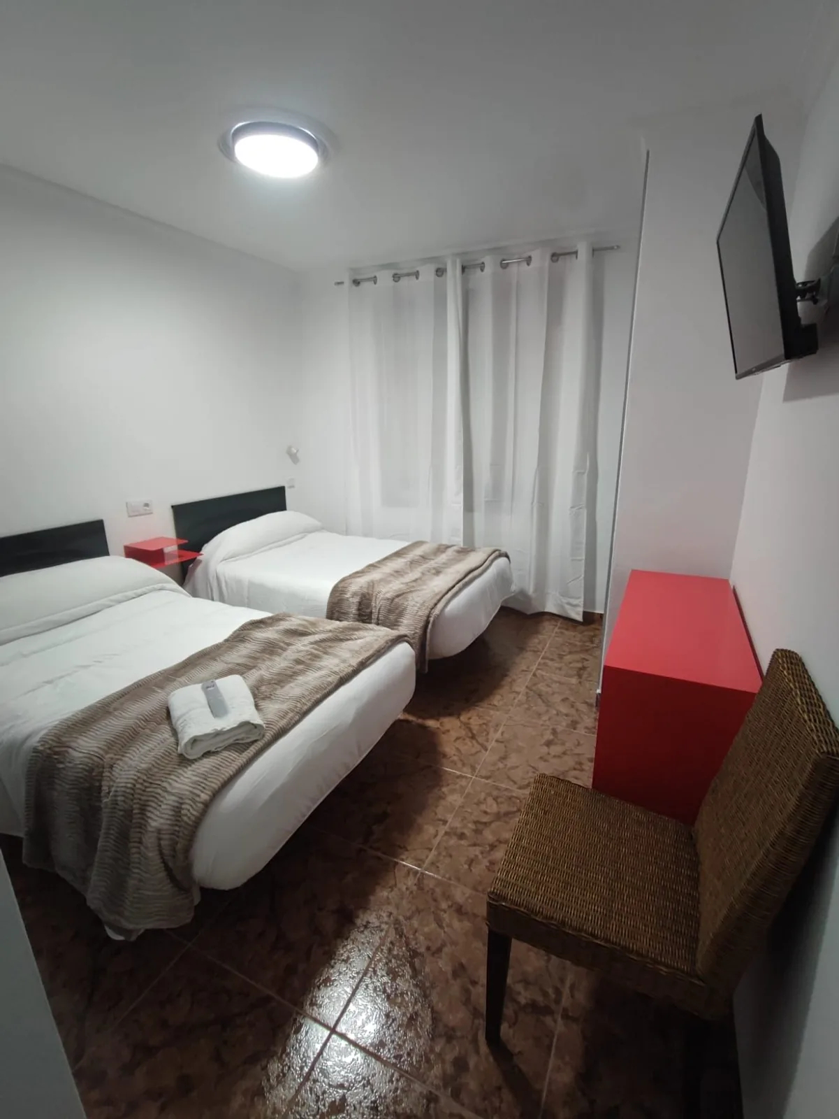 Habitación doble con dos camas, televisor y mobiliario en tonos rojos